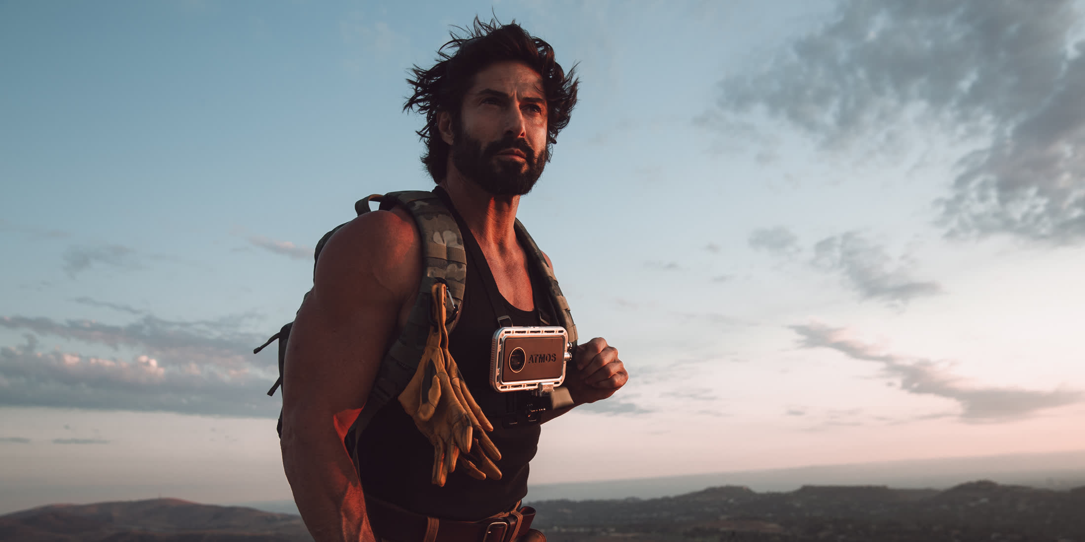 Man on a mountain ridge at sunset holding a phone in an Atmos rugged case